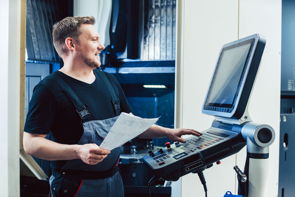 Machine operator holding a drawing while programming a CNC lathe